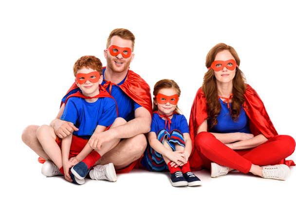 super family in costumes sitting together and smiling at camera isolated on white - Foto, Imagen