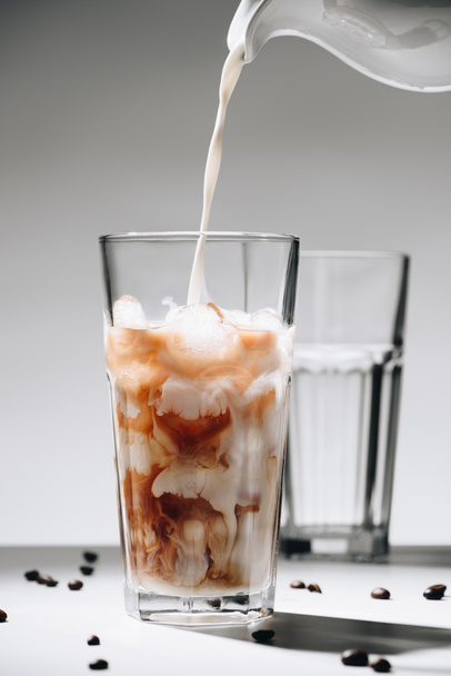 Nahaufnahme des Einfüllens von Milch in ein Glas Eiskaffee vor grauem Hintergrund - Foto, Bild