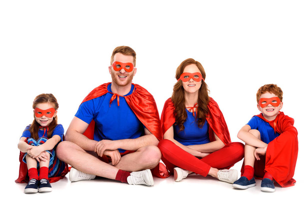 happy family of superheroes sitting together and smiling at camera isolated on white - Fotografie, Obrázek