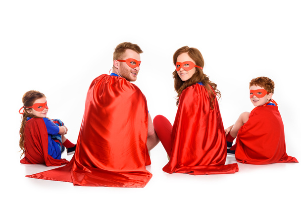 back view of family of superheroes sitting together and looking at camera isolated on white - Photo, Image