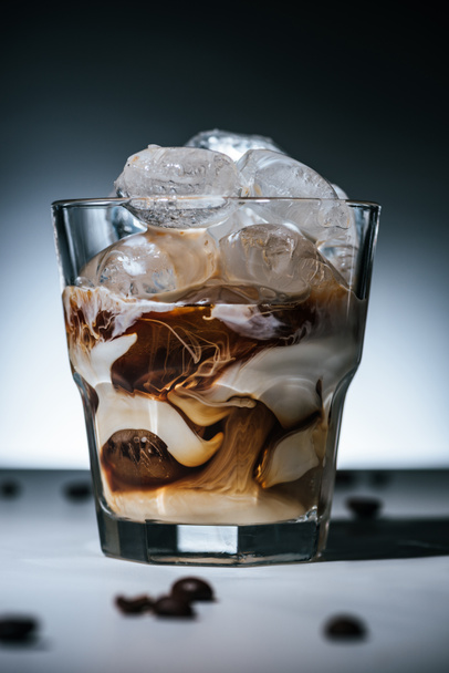 primer plano vista de café elaborado en frío con cubitos de hielo y granos de café tostados en la mesa en vidrio sobre fondo oscuro
 - Foto, Imagen