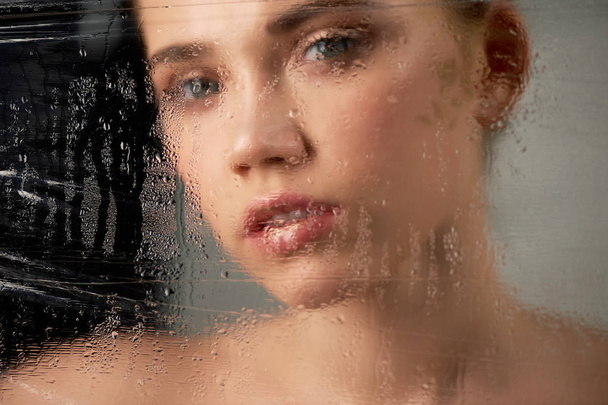 Portrait of young beautiful girl in Studio, with professional makeup.Beauty shooting. In the face of a transparent glass with water droplets. Hydration of the skin - Φωτογραφία, εικόνα