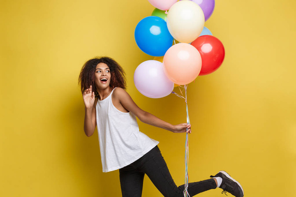 Concepto de celebración - Primer plano Retrato feliz joven hermosa mujer africana con camiseta blanca corriendo con globo de fiesta de colores. Fondo de estudio Pastel amarillo
 - Foto, imagen