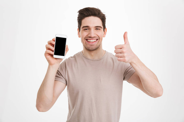 Photo of brunette guy in beige t-shirt holding cell phone with c - Valokuva, kuva