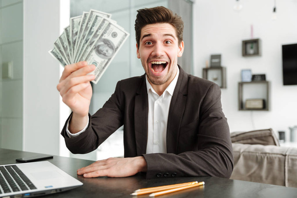 Excited young businessman showing money using laptop computer. - Foto, Imagem