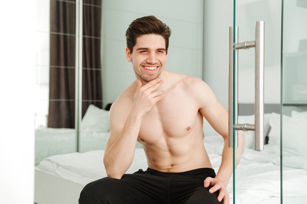 Happy cheerful naked man sitting on bed - Fotó, kép