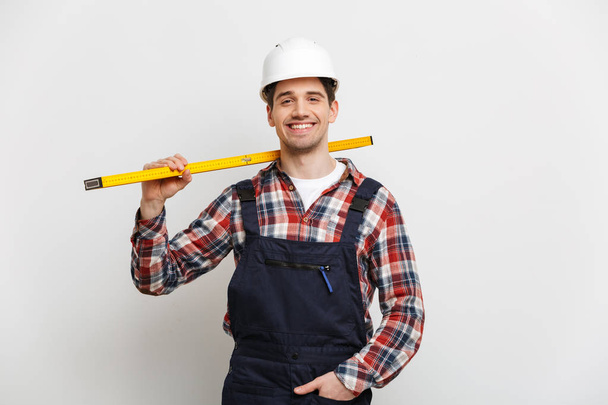 Smiling male builder in protective helmet holding level tool - Foto, Bild