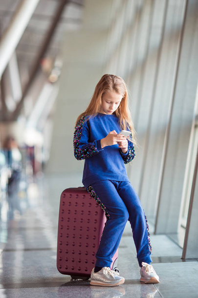 Adorable little girl in airport near big window playing with her phone - Fotó, kép