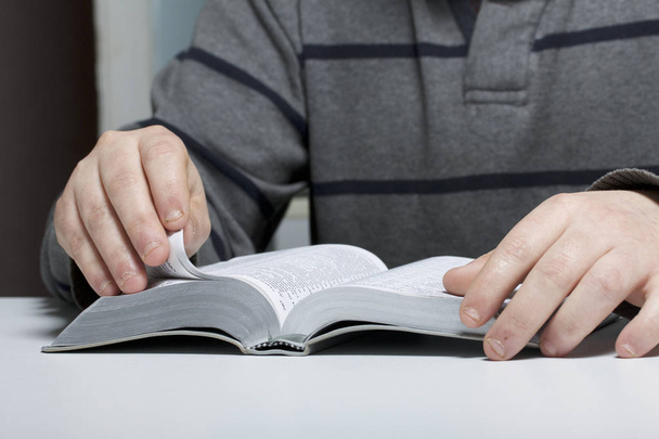 Mladý muž čte Bibli s plátkem stříbra u stolu. - Fotografie, Obrázek