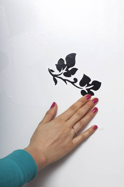 The girl glues the cut out elements from self-adhesive paper, to mask the defects of the white door. - Foto, afbeelding