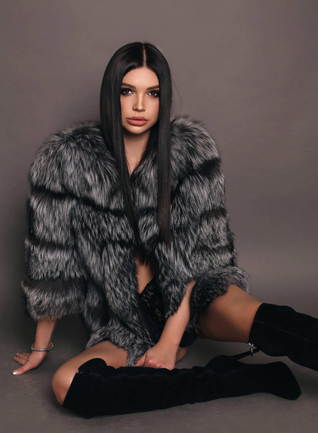 fashion photo of beautiful woman with dark hair in luxurious fur coat and jackboots posing in studio - Фото, изображение
