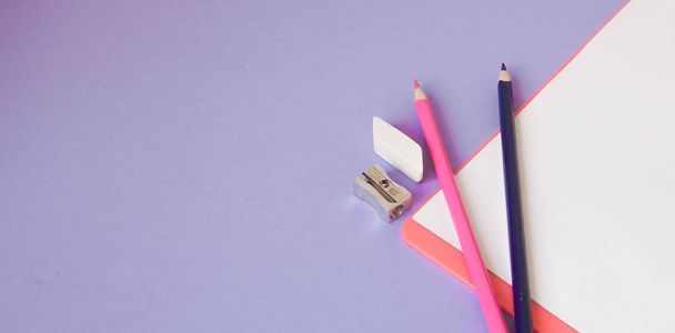 Multicolored, bright, colorful pencils are located at the bottom at an angle and a notebook for your text on a violet background - Foto, imagen