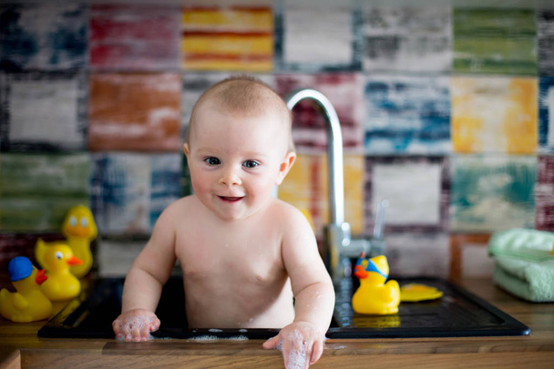 Cute snmiling baby taking bath in kitchen sink. Child playing wi - Photo, Image