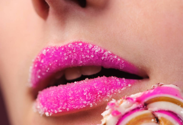 sexy girl's lips with a lollipop over pink background in studio - Foto, afbeelding
