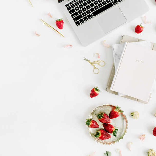 Area di lavoro femminile con laptop, notebook, rossetto, fragola fresca e cruda su sfondo bianco. Posa piatta, vista dall'alto
. - Foto, immagini