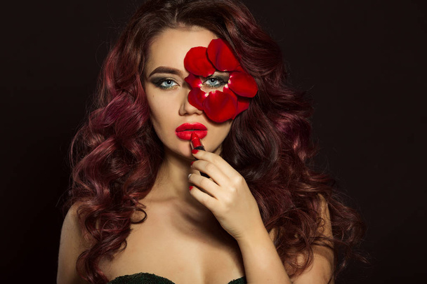 Portrait of beautiful luxury sexy woman with creative makeup and red rose petals of her face is holding lipstick - Фото, изображение