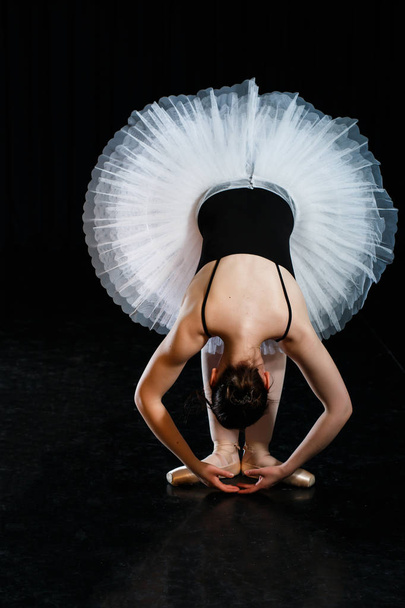 Girl ballerina posing and performing dance elements in bright scenic light on a black background - Φωτογραφία, εικόνα