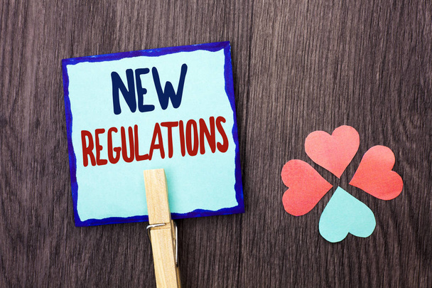 Handwriting text writing New Regulations. Concept meaning Change of Laws Rules Corporate Standards Specifications written on Sticky Note Paper Holding With Clip on the wooden background Hearts. - Photo, Image