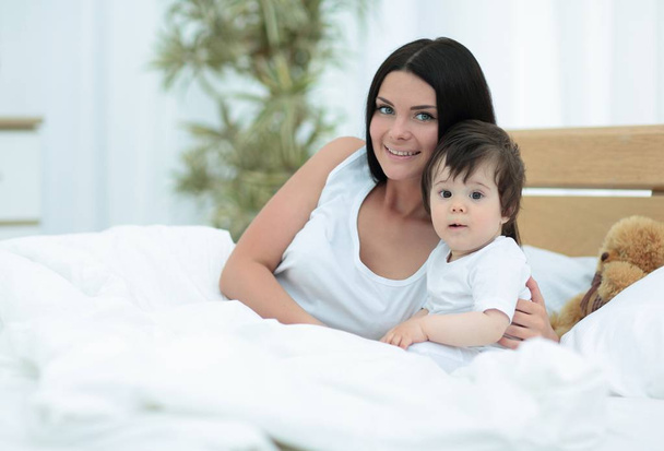 Портрет красивой матери с ребенком в спальне
 - Фото, изображение