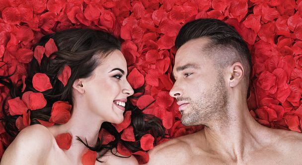 Romantic couple laying on rose petals - Фото, изображение