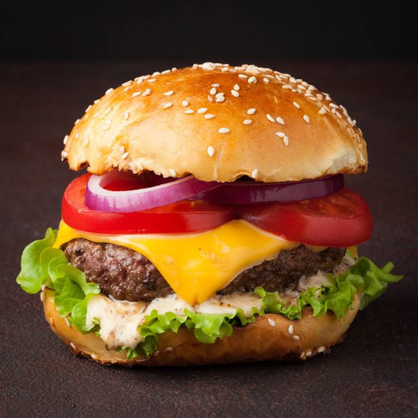 Zbliżenie: pyszne świeże domowe burger z sałatą, serem, cebuli i pomidorów na ciemnym tle. Fast food i jedzenie koncepcja - Zdjęcie, obraz