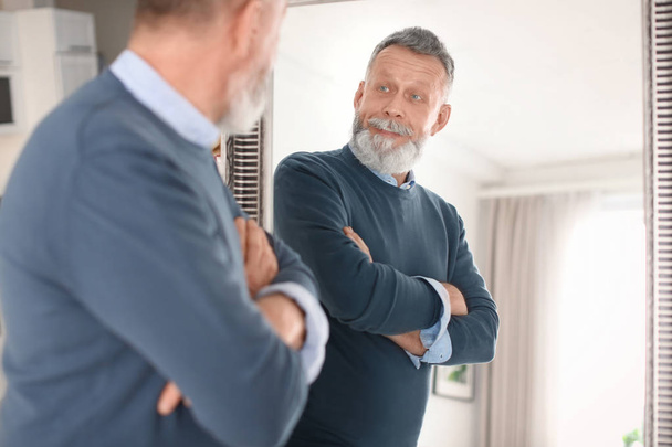 Mature man looking in mirror at home - Foto, Bild