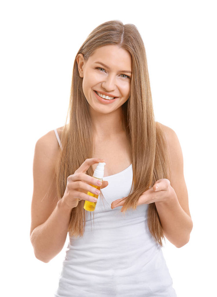 Young woman applying oil onto hair on white background - Foto, imagen