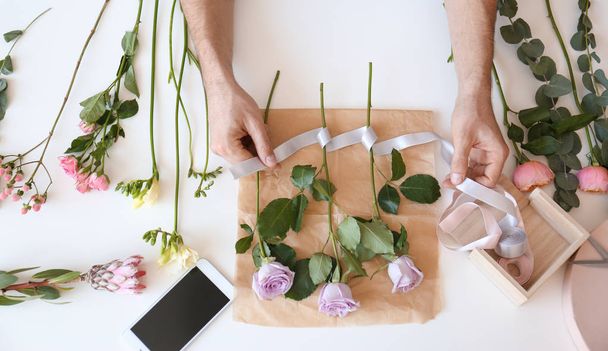 Male florist creating beautiful bouquet at table, top view - 写真・画像
