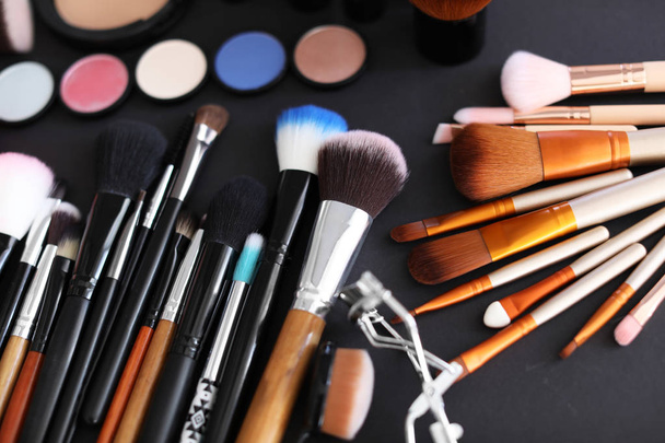 Different makeup brushes and cosmetic products on black background - Photo, Image