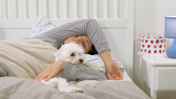 Woman sleeping in the morning hugging little puppy dog in bed - Кадри, відео