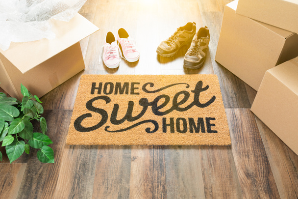 Otthon, édes otthon üdvözlő szőnyeg, mozgó dobozok, női és férfi cipő és növény a kemény fa padló. - Fotó, kép