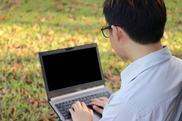 Hát Nézd, látszó laptop számítógép-val egy üres képernyő-elmosódott fű háttér fiatalember. - Fotó, kép