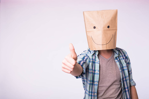 Unknown man showing thumbs up with a paper bag on his head on white background - Foto, Bild