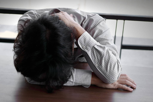 Väsynyt ylityöllistetty nuori aasialainen liikemies makaa kasvot alaspäin toimistopöydällä
 - Valokuva, kuva