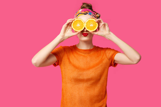 Young woman on a pink background holds a cut orange in her hands and laughs. Colour obsession concept.  Minimalistic style. Stylish Trendy - Foto, imagen