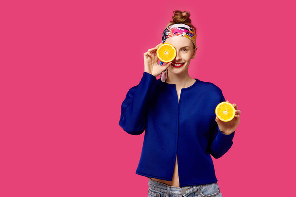 Jovem mulher em um fundo rosa segura uma laranja de corte em suas mãos e ri. Conceito de obsessão a cores. Estilo minimalista. Elegante moda
 - Foto, Imagem