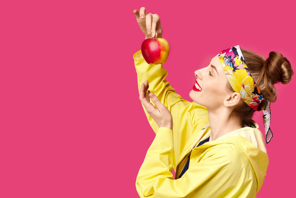 Młoda kobieta na tle różowy i żółty płaszcz trzyma jabłko w jej ręce. Koncepcja zdrowe odżywianie i sport. Kolor koncepcja obsesji. Minimalistyczny styl. Elegancki, modny - Zdjęcie, obraz
