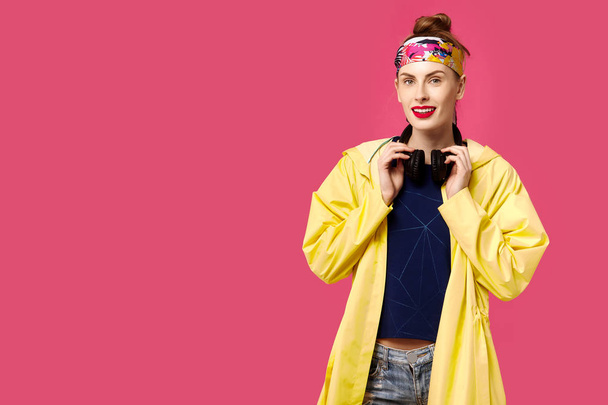 Young beautiful woman on a pink background and a yellow coat listening to music through wireless headphones. Concept of healthy nutrition and sports.  Colour obsession concept.  Minimalistic style. St - Photo, Image
