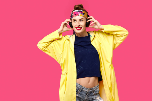 junge schöne Frau auf rosa Hintergrund und gelbem Mantel, die über drahtlose Kopfhörer Musik hört. Konzept der gesunden Ernährung und Sport. Farbbesessenheit. Minimalistischer Stil. st - Foto, Bild