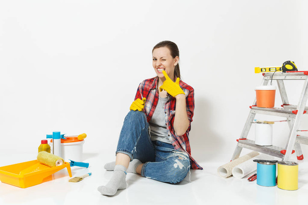 Spaß hübsche Frau in lässiger Kleidung sitzt auf dem Boden mit gelben Handschuhen, Instrumente für die Renovierung Wohnung isoliert auf weißem Hintergrund. Tapeten-Zubehör für Malwerkzeuge. Heimkonzept reparieren - Foto, Bild