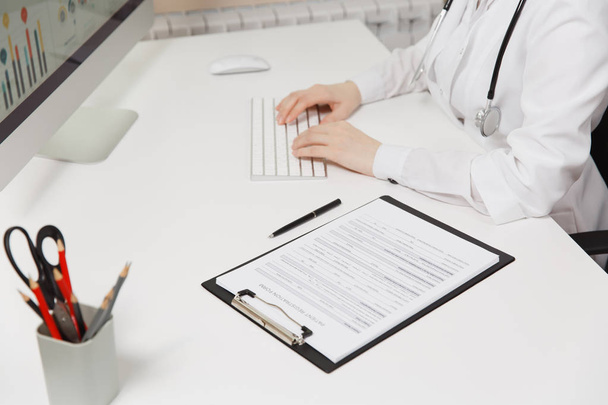 Close up woman sitting at desk, working with medical documents, clipboard with disease history in light office in hospital. Female doctor in consulting room. Healthcare, medicine concept. Copy space. - Фото, зображення