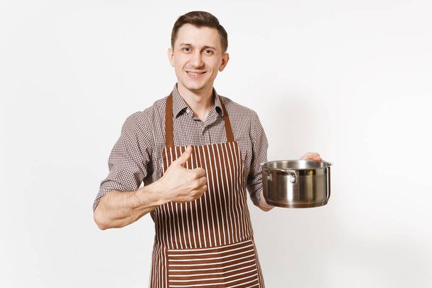 Chef Man w paski brown fartuch, trzymając pusty rondel srebrny stal aluminium błyszczący, patelni lub garnka na białym tle. Mężczyzna gospodyni lub houseworker. Przybory kuchenne, naczynia, kuchnia koncepcja. - Zdjęcie, obraz