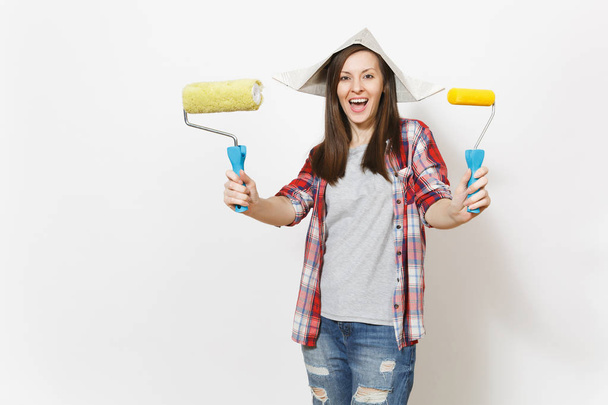 Young overjoyed beautiful woman in casual clothes and newspaper hat holding rollers for wall painting isolated on white background. Instruments for renovation apartment room. Repair home concept. - Fotoğraf, Görsel