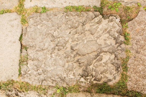 Trottoir geplaveid met grote stenen en gras groeit tussen hen - Foto, afbeelding