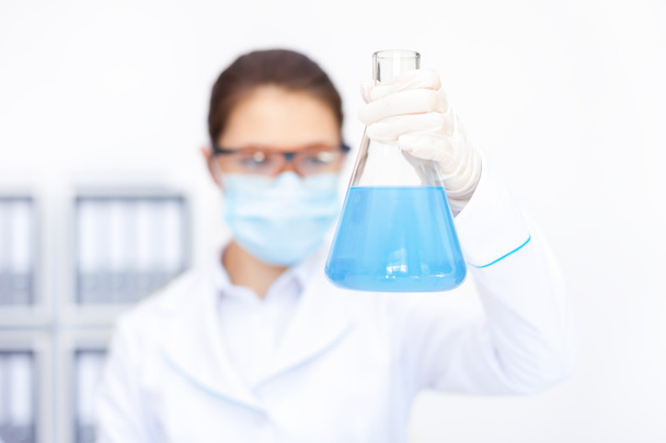 female researcher observing liquid in flask - Фото, изображение