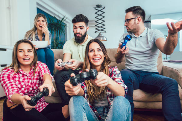 Grupo de amigos juegan videojuegos juntos en casa, divirtiéndose. - Foto, Imagen