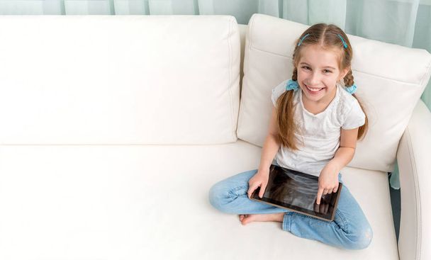 cheerful little girl with tablet on her legs looking at camera - Foto, Imagem