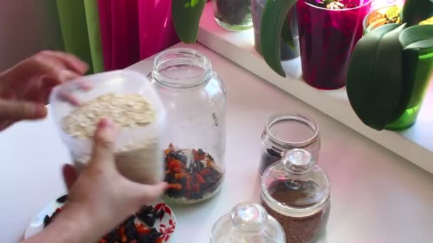 The man mixes in a glass jar a dried fruit, oat flakes to get muesli - Felvétel, videó