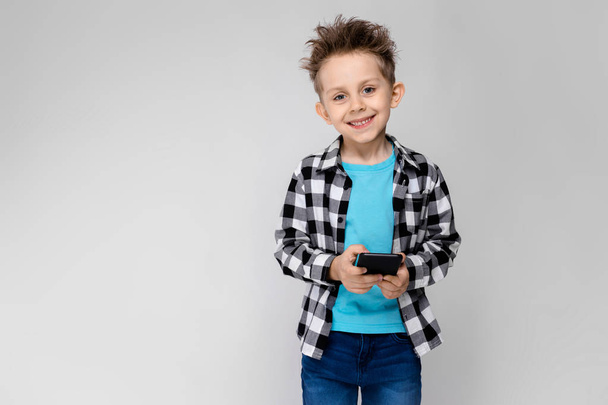 Szép óvodás kaukázusi fiú alkalmi ruhában pózol smartphone mutatja a különböző kifejezések fehér falon a stúdió. - Fotó, kép