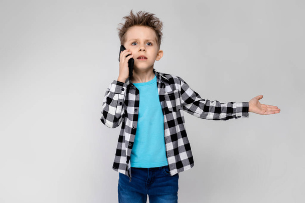 Szép óvodás kaukázusi fiú alkalmi ruhában pózol smartphone mutatja a különböző kifejezések fehér falon a stúdió. - Fotó, kép